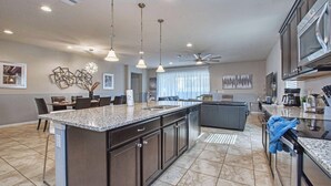 A spacious kitchen with a large island, dark cabinetry, and modern lighting fixtures. - Home 8 Bdrm at Windsor Westside With Top Amenities (Kissimmee)