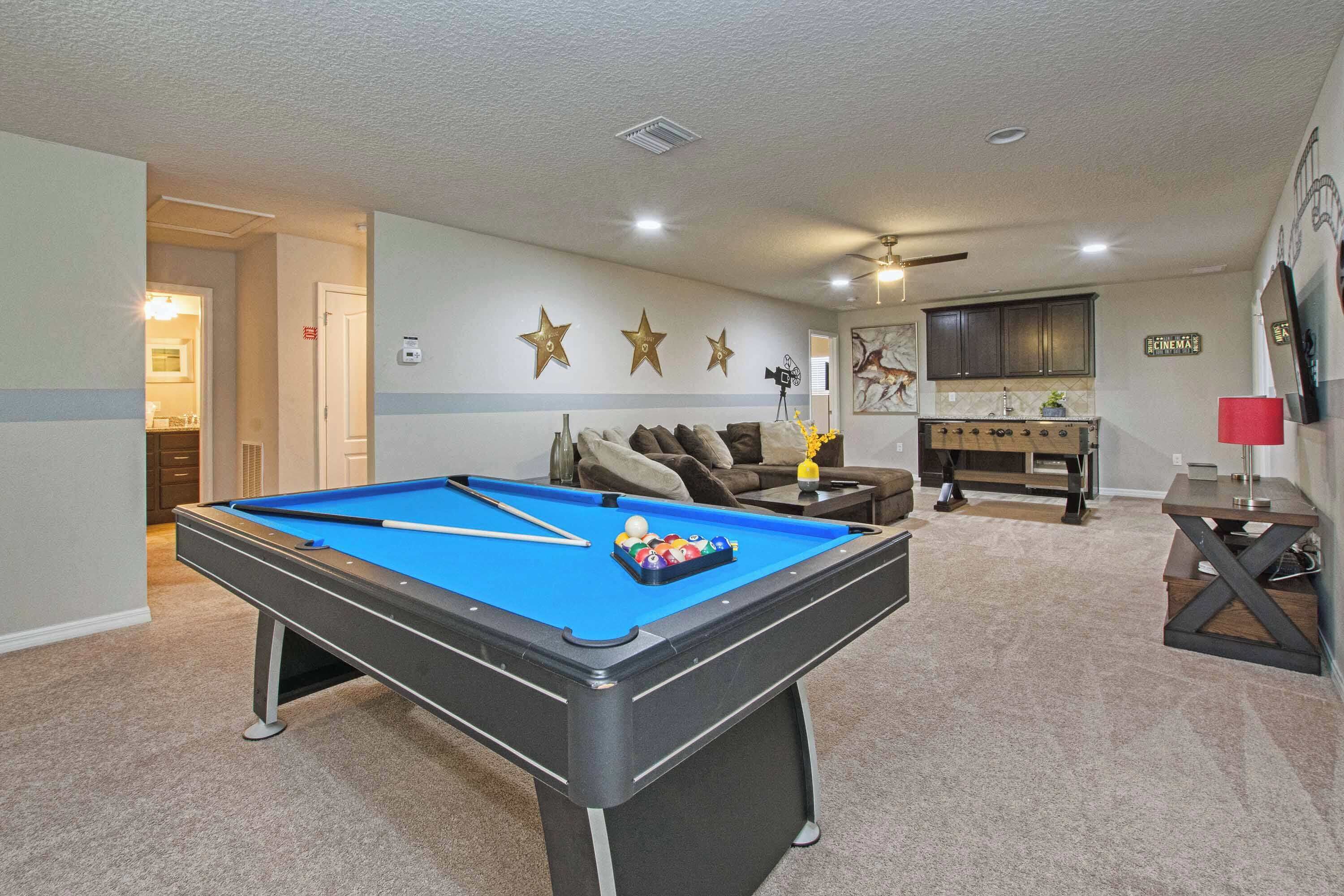 A pool table in a room with a ceiling fan, a sofa, and a television.