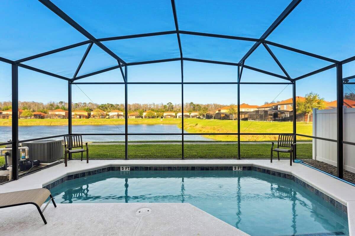 A covered outdoor swimming pool with a view of a lake and houses in the background.
