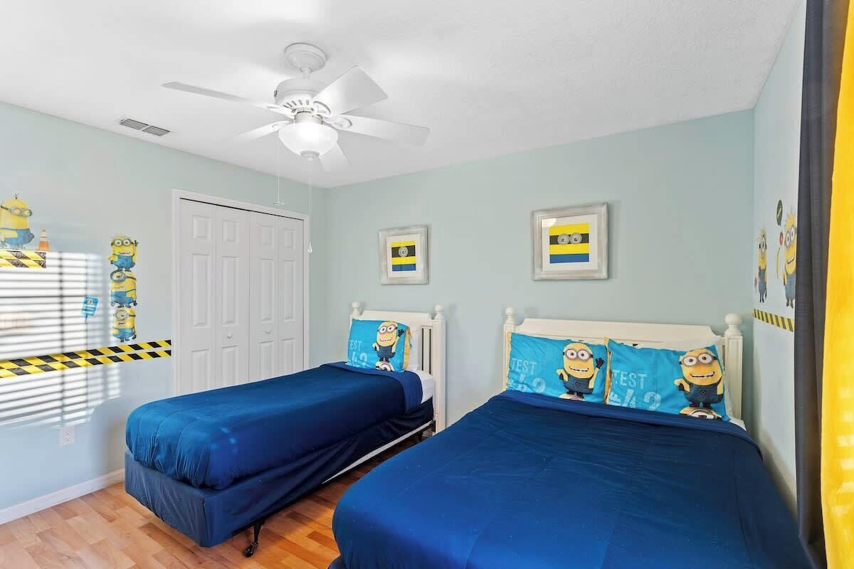A bedroom with two beds, a ceiling fan, and Minion-themed decor.
