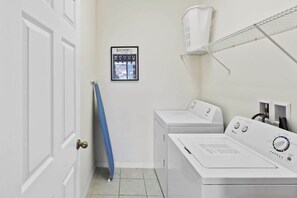 A laundry room with two white washers and dryers, a blue towel rack, a framed laundry chart, and a white ceiling fan. - Lake View and Private Pool 4BR at Bella Vida (Kissimmee)