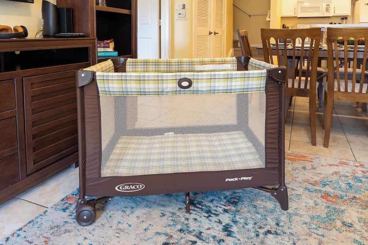 Ein Graco Pack 'n Play Babybett in einem Raum mit Holzmöbeln und einem gemusterten Teppich.