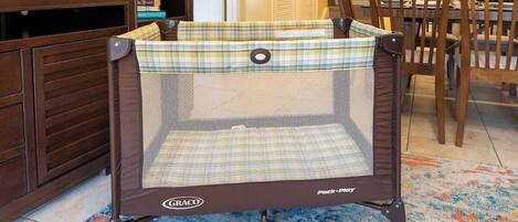 Ein Graco Pack 'n Play Babybett in einem Raum mit Holzmöbeln und einem gemusterten Teppich.