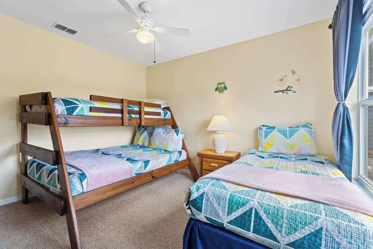 Ein Schlafzimmer mit zwei Etagenbetten, einem Deckenventilator, einer Nachttischlampe und einem Fenster mit Vorhängen.