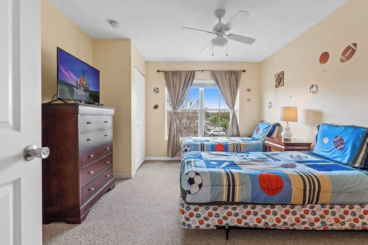 Een slaapkamer met een bed, een dressoir, een televisie, een plafondventilator en sportieve decoratie.
