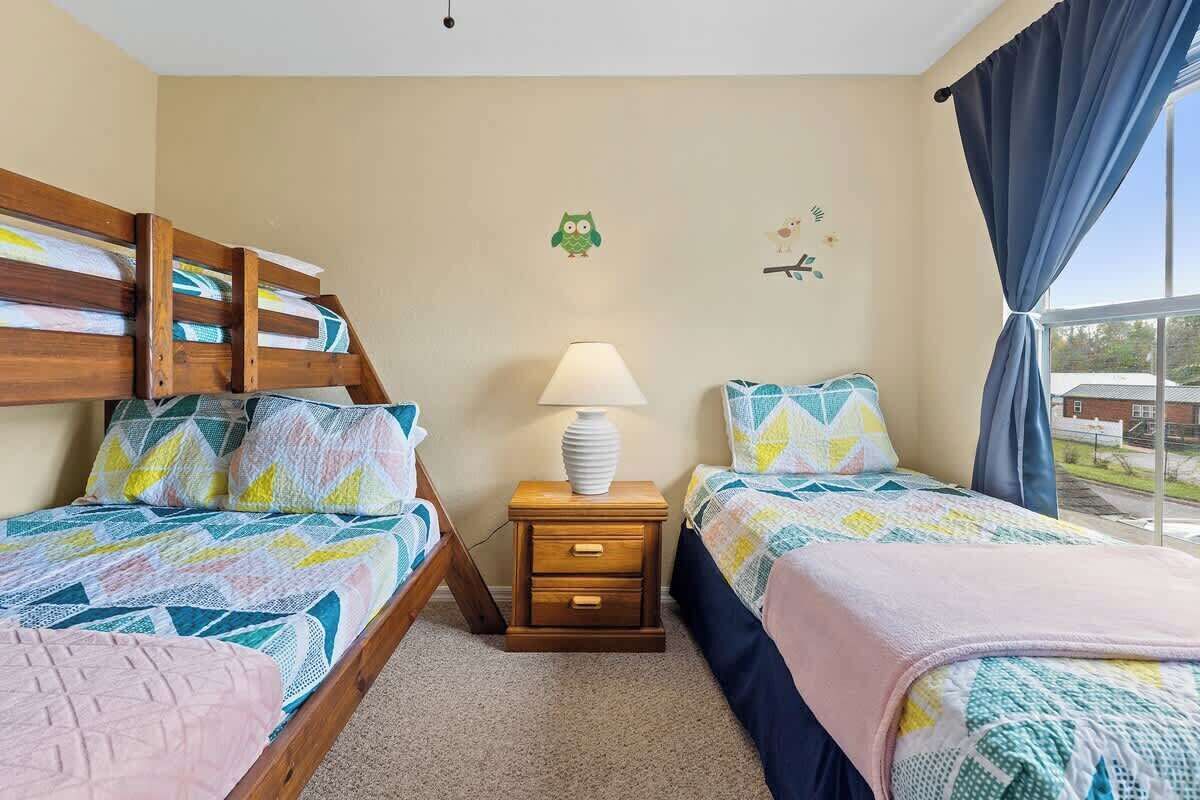 A bedroom with two bunk beds, a bedside table with a lamp, and a window with curtains.