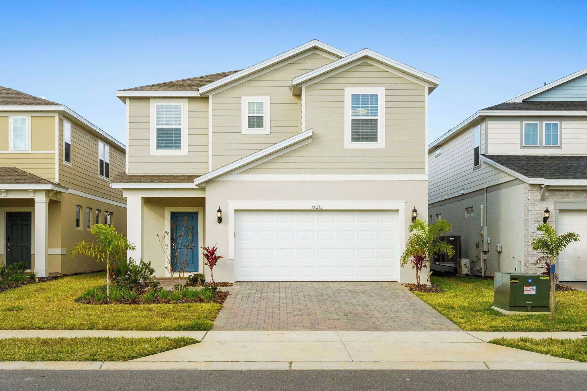 A two-story residential house with a garage, a front yard with landscaping, and a clear sky.