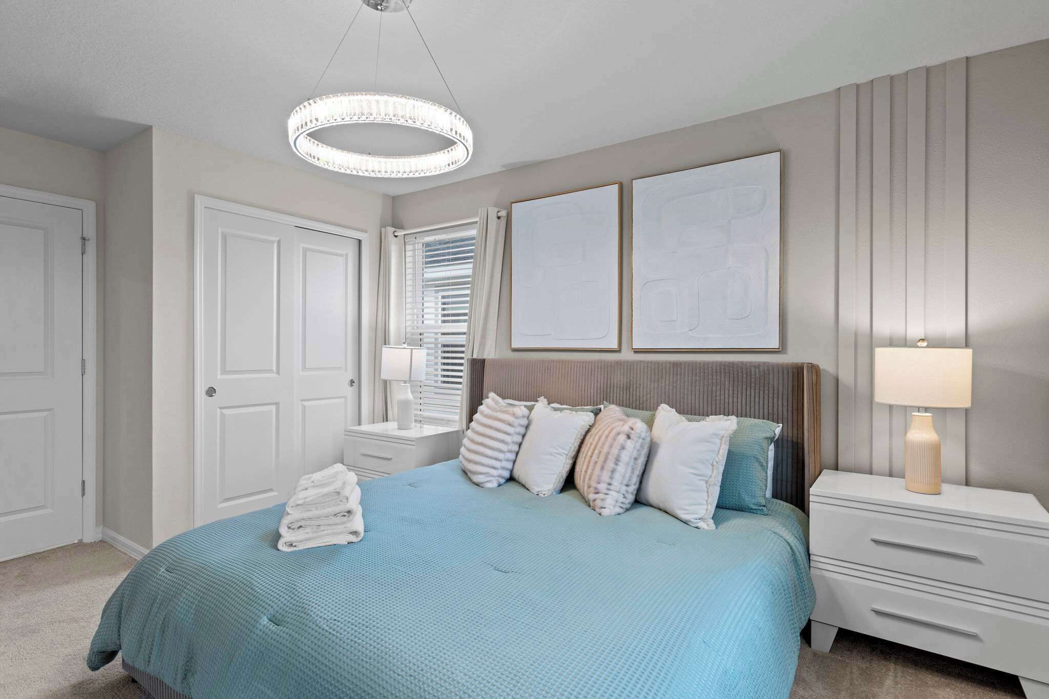 Une chambre à coucher comprenant un lit, des tables de chevet, un luminaire suspendu et une porte.