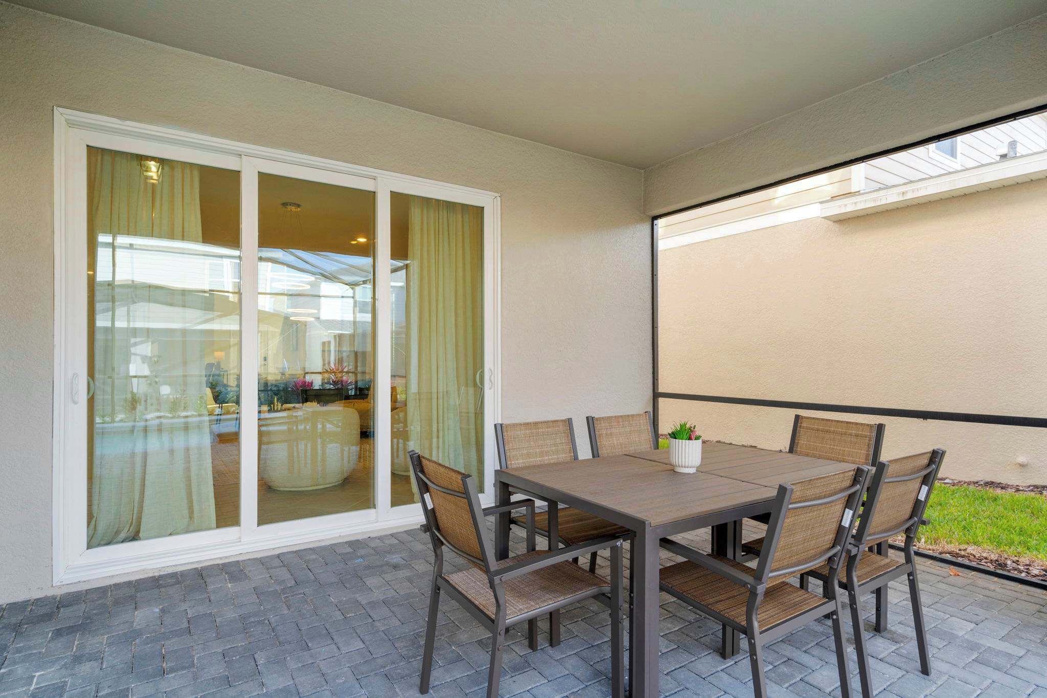 Um pátio com mesa e cadeiras, uma porta de correr de vidro e vista para uma casa.