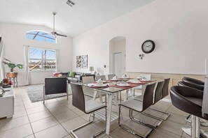 A dining area with a glass table, metal chairs, and a clock on the wall. - Ground Floor Gathering up to 9 Guests Bl387 (Kissimmee)