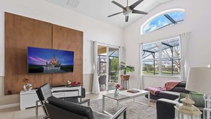 Een moderne woonkamer met een flatscreen-tv, een plafondventilator, een groot raam en een schuifpui naar een buitenruimte.