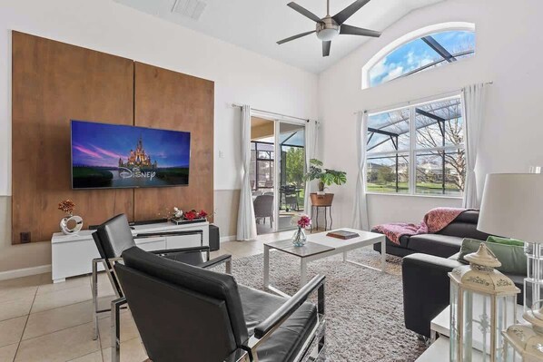 A modern living room with a flat-screen TV, a ceiling fan, a large window, and a sliding glass door leading to an outdoor area. - Ground Floor Gathering up to 9 Guests Bl387 (Kissimmee)