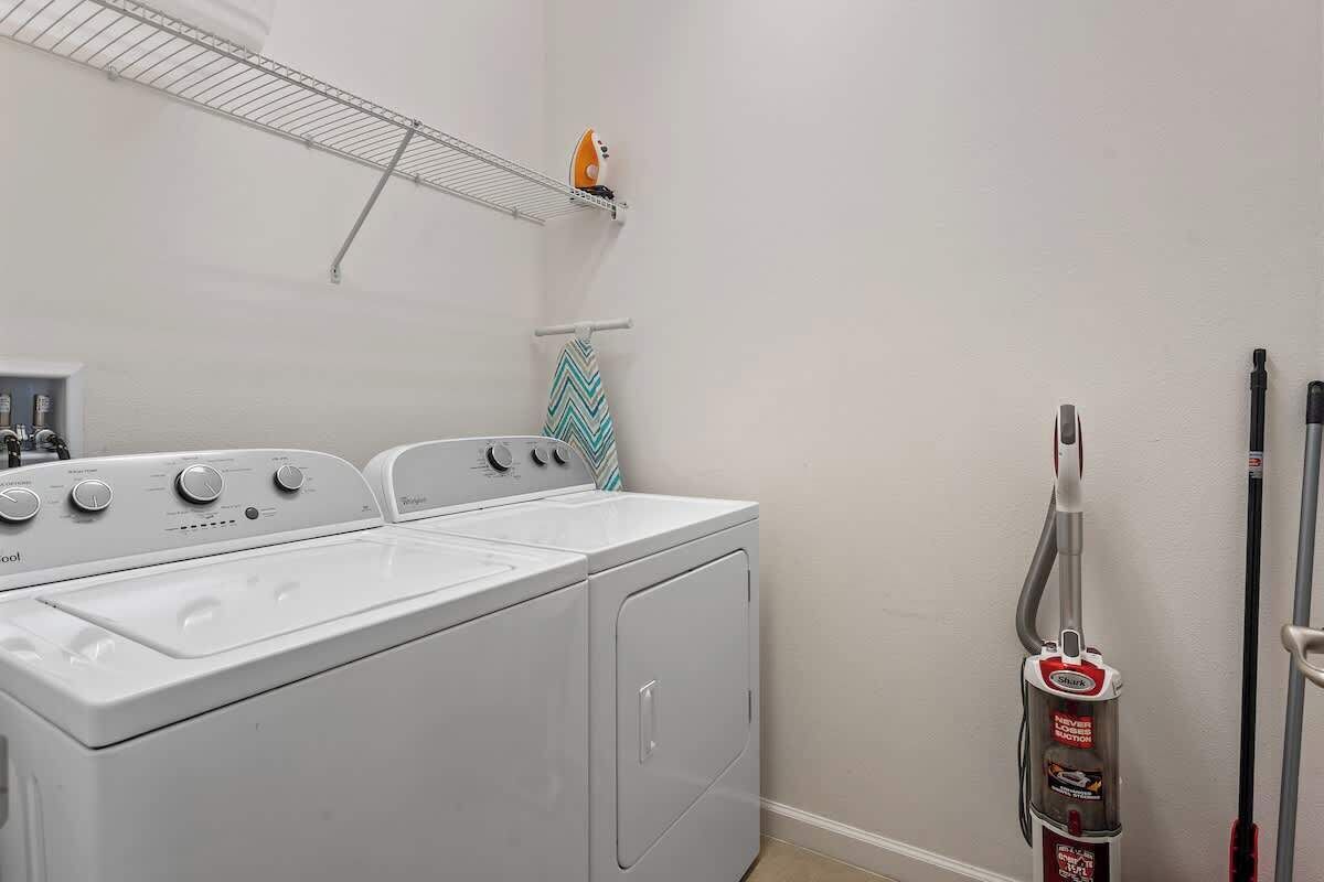 A laundry area with a front-loading washer and dryer, a metal drying rack, and a vacuum cleaner.