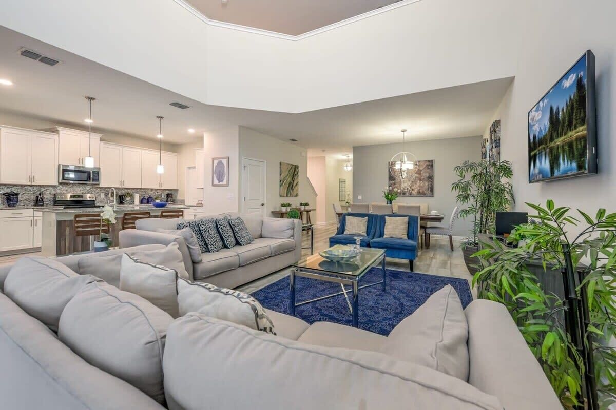 A modern living room with a sofa, coffee table, and a TV. There is a kitchen area with cabinets and appliances.