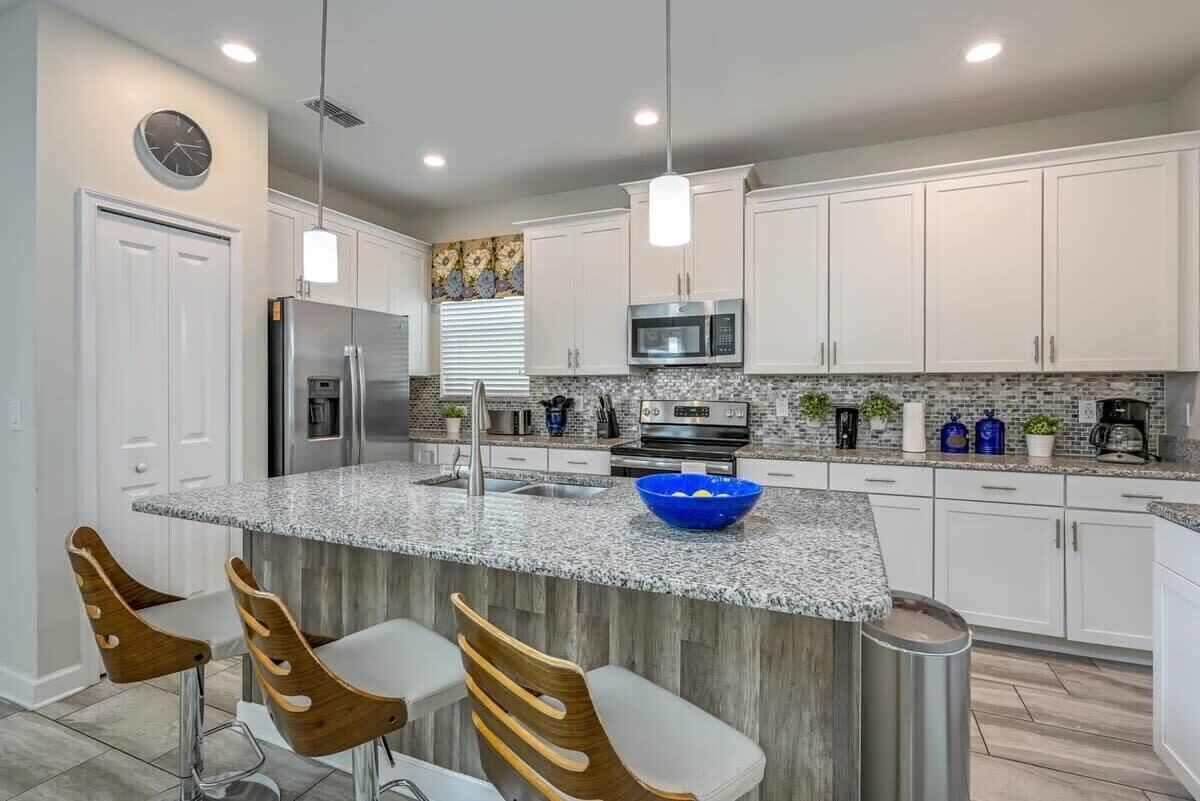 Una cocina moderna con armarios blancos, encimeras de granito, un refrigerador de acero inoxidable y un tazón azul en la isla.