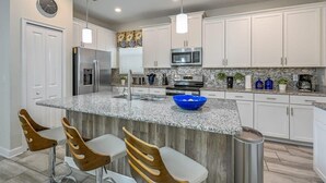 Eine moderne Küche mit weißen Schränken, Granit Arbeitsplatten, einem Edelstahlkühlschrank und einer blauen Schüssel auf der Kochinsel.
