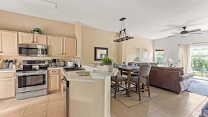 A modern kitchen with a central island, stainless steel appliances, and a dining area with a brown sofa and table. - Harry Potter Themed 3 BR (Kissimmee)