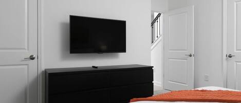 Une chambre à coucher avec un lit, une commode noire, un téléviseur fixé au mur et des portes blanches.