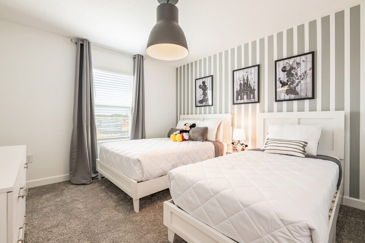 A hotel room with two beds, a desk, a window with curtains, and wall art.