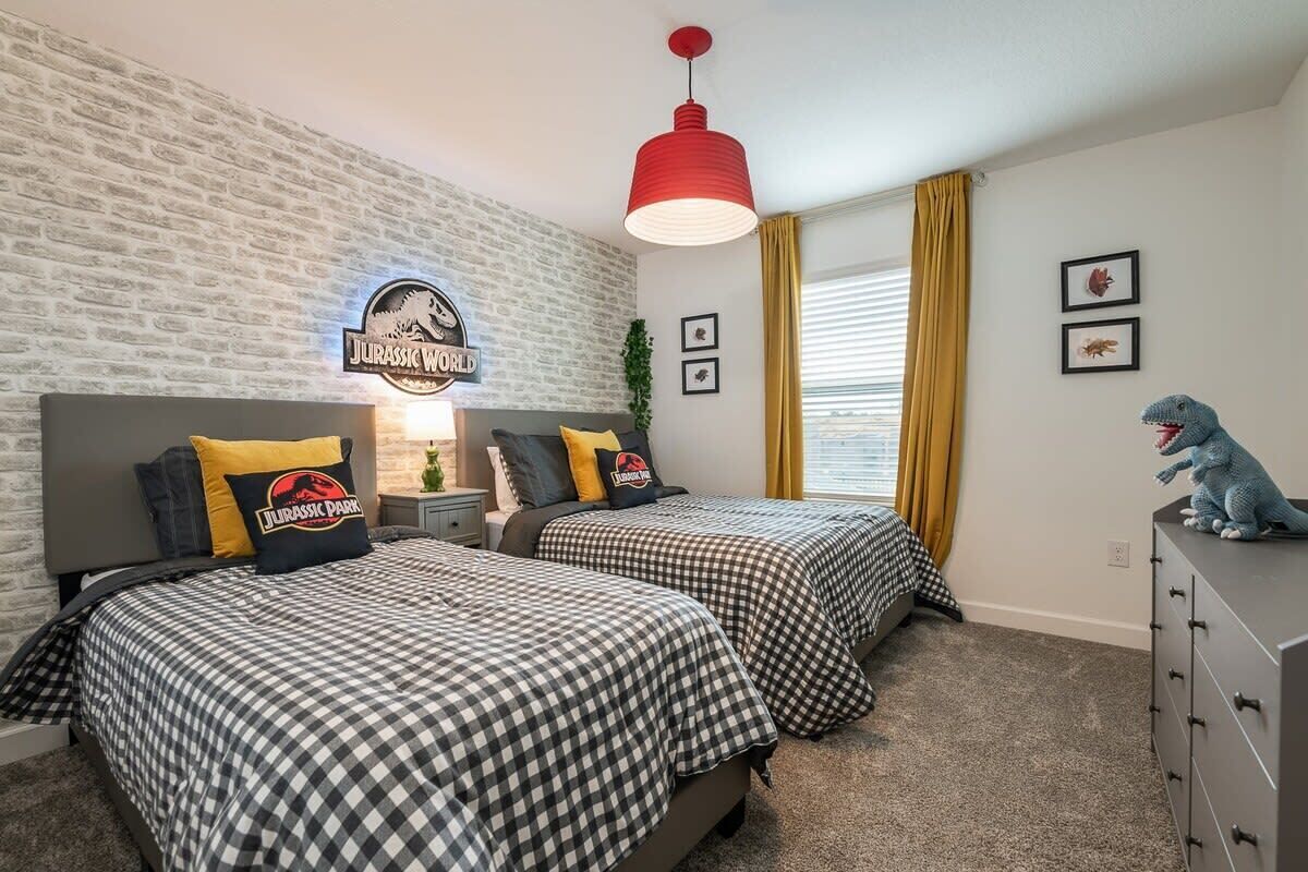 Une chambre avec deux lits, un luminaire suspendu rouge, un mur en briques et une fenêtre avec des rideaux jaunes.