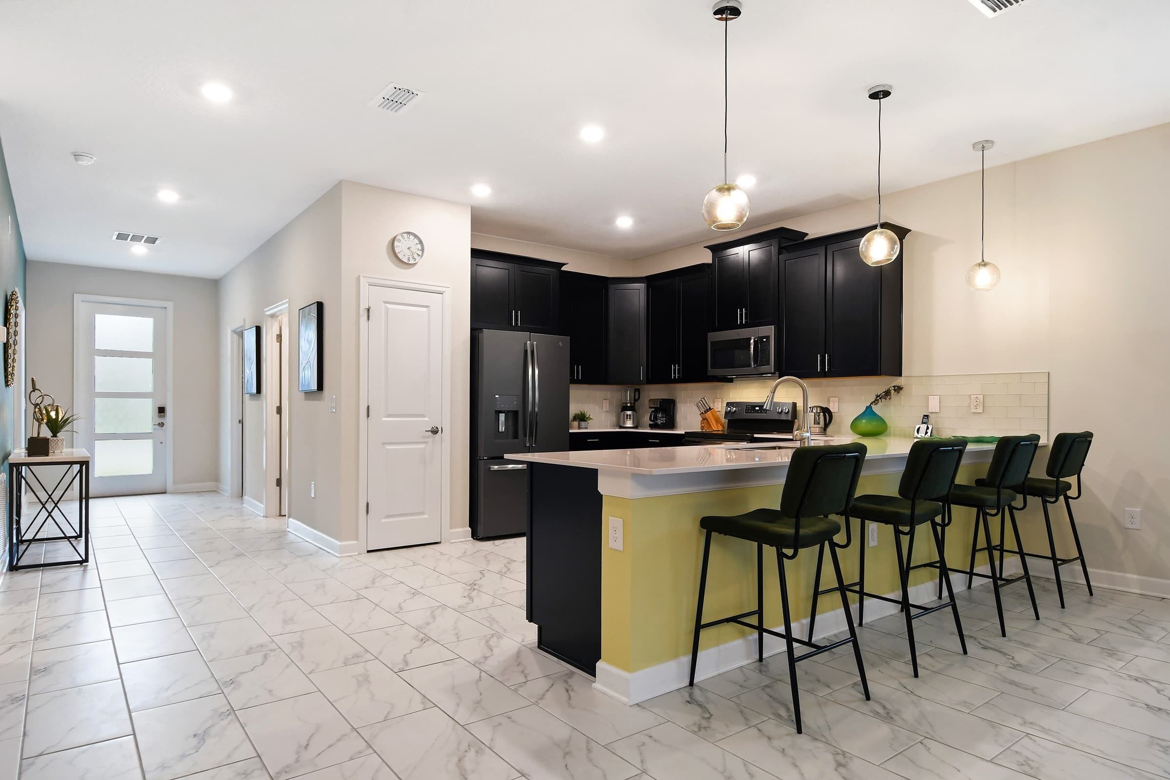A modern kitchen with dark cabinets, a central island with bar stools, and recessed ceiling lights.
