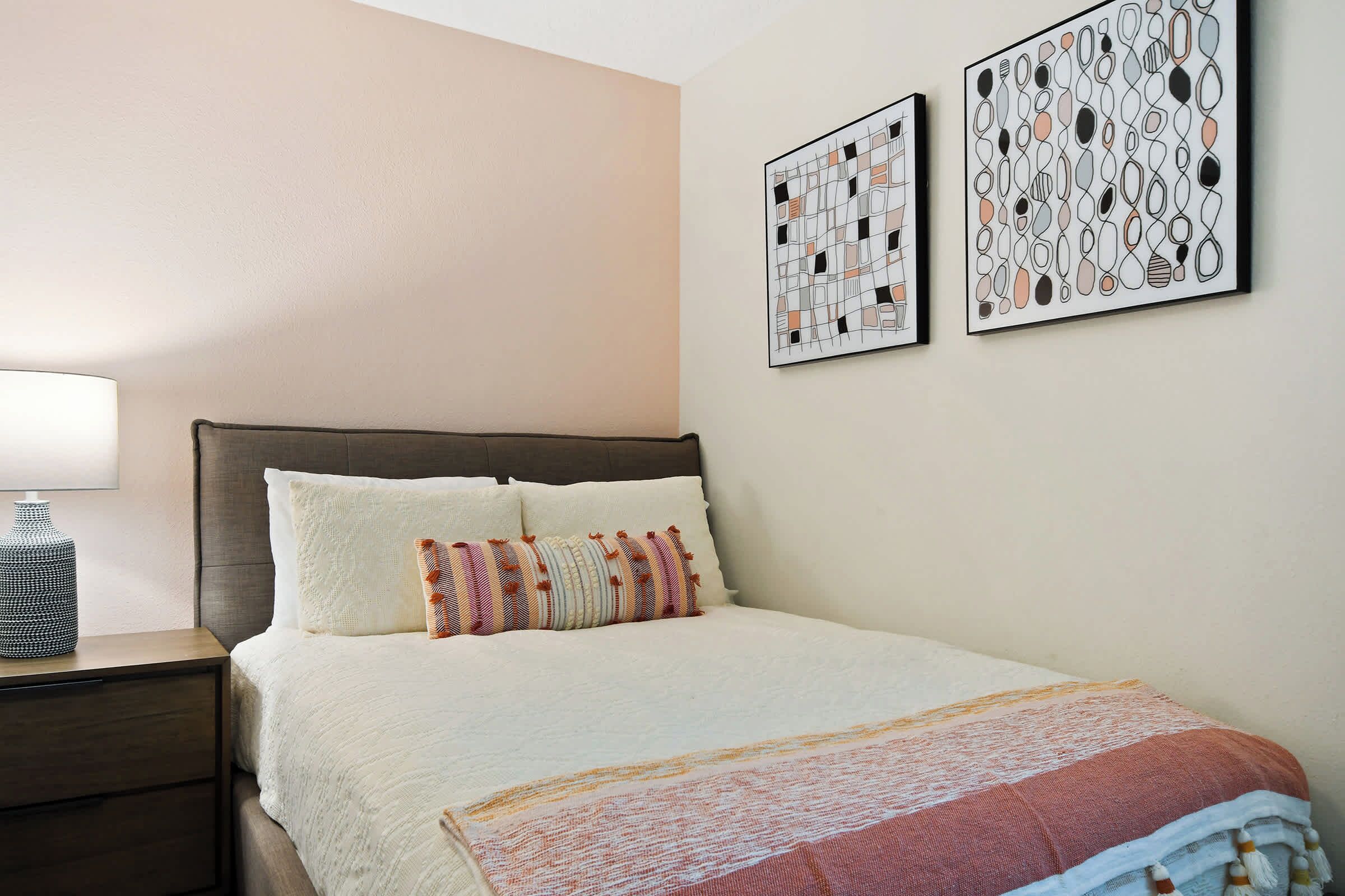 A bedroom with a bed, nightstand, and two wall-mounted artworks.