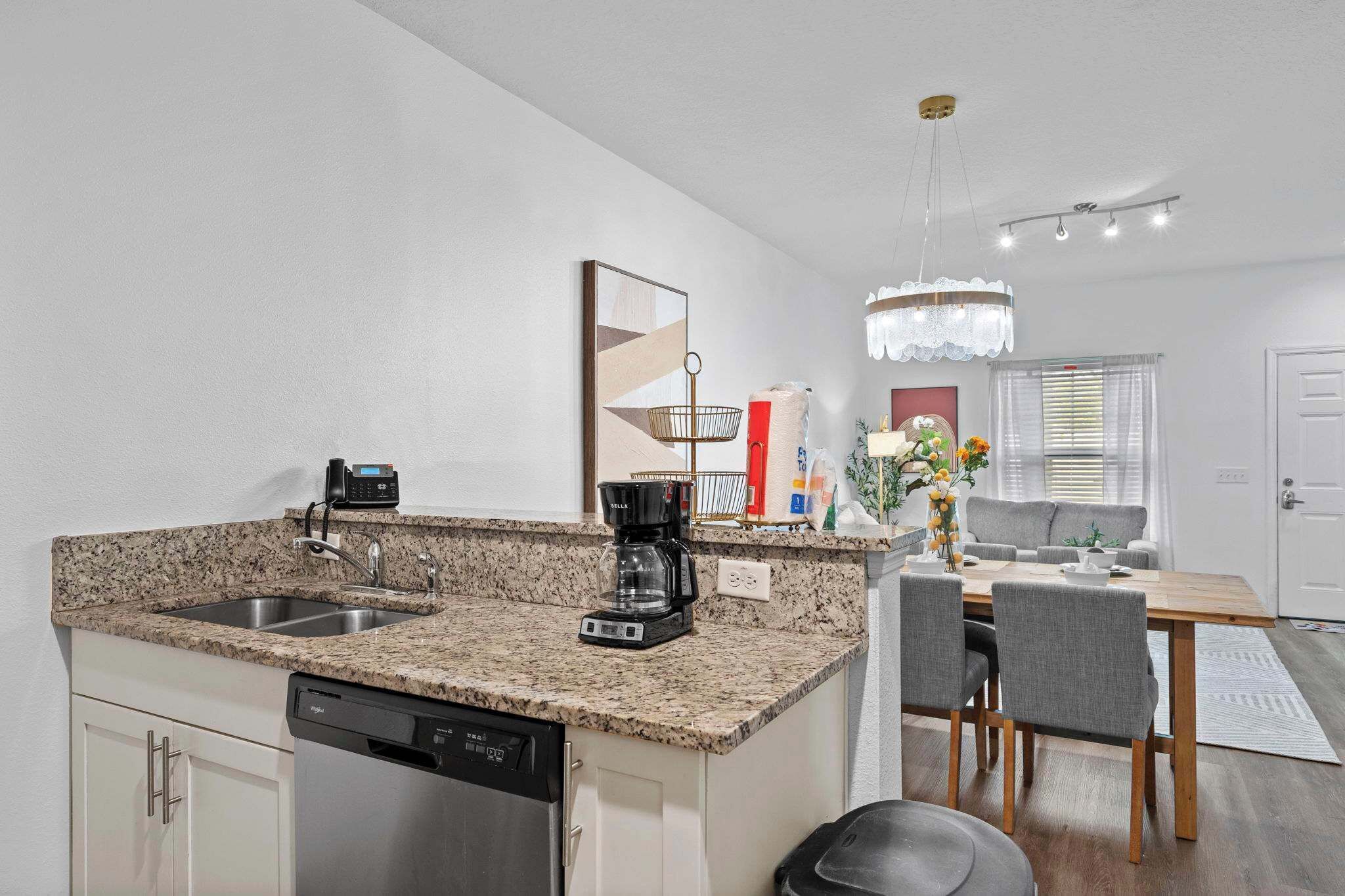 A kitchen with granite countertops, a coffee maker, and a dishwasher. There is a dining area with a table and chairs.