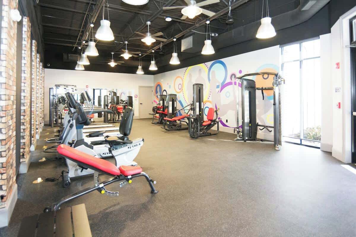 A gym with exercise equipment, a brick wall, and a colorful mural.
