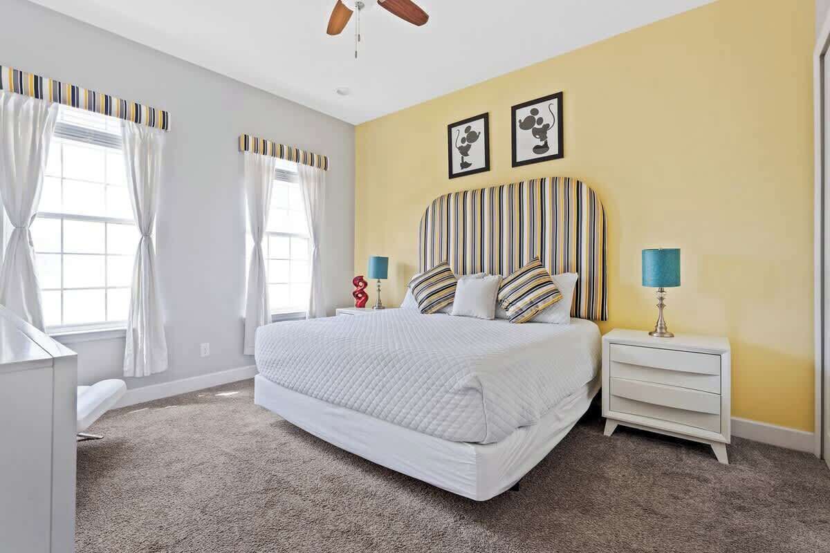 A bedroom with a large bed, two bedside tables, a ceiling fan, and a window with curtains.