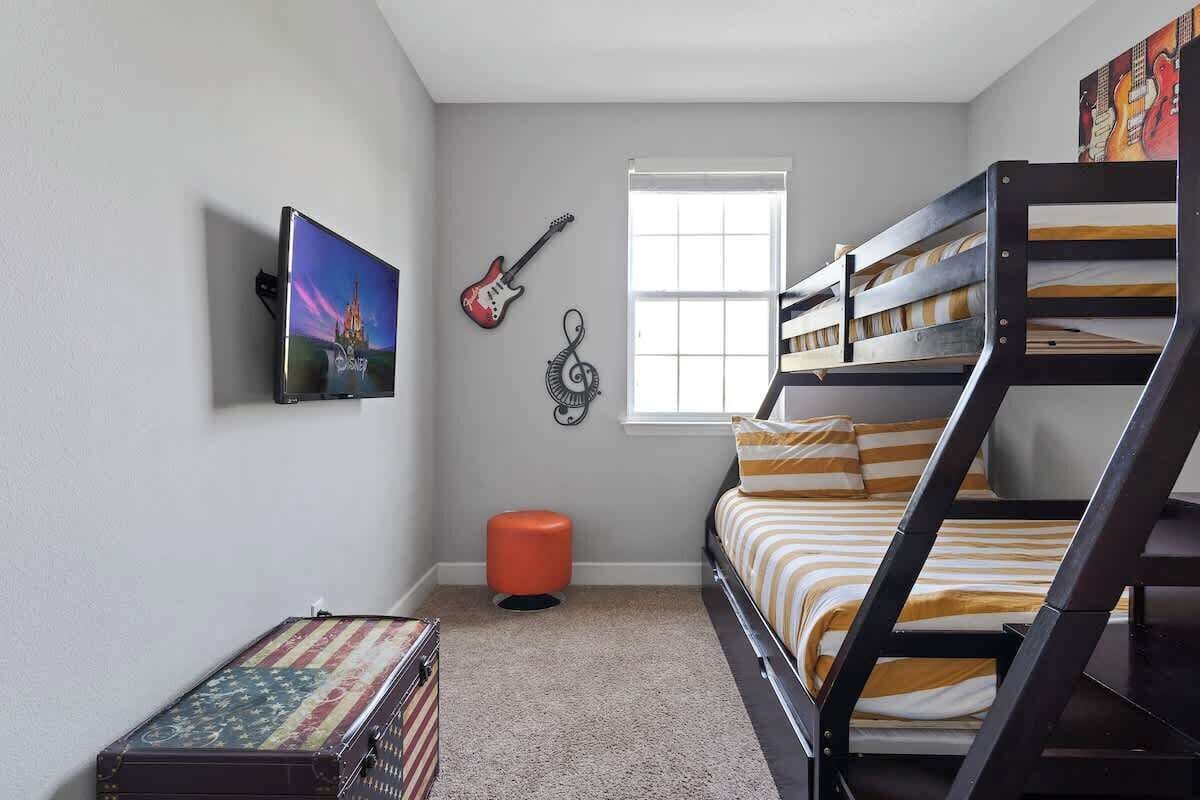 Una camera da letto con letti a castello, una televisione, chitarre e una valigia.