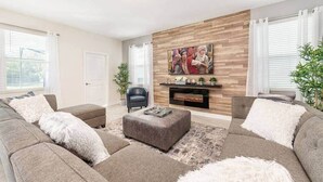 A living room with a fireplace, a sofa set, a coffee table, and a painting on the wall. - Modern Marvel-spacious, Themed, Fun-filled (Kissimmee)