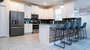 A modern kitchen with white cabinets, stainless steel appliances, and a central island with bar stools. - Modern Marvel-spacious, Themed, Fun-filled (Kissimmee)