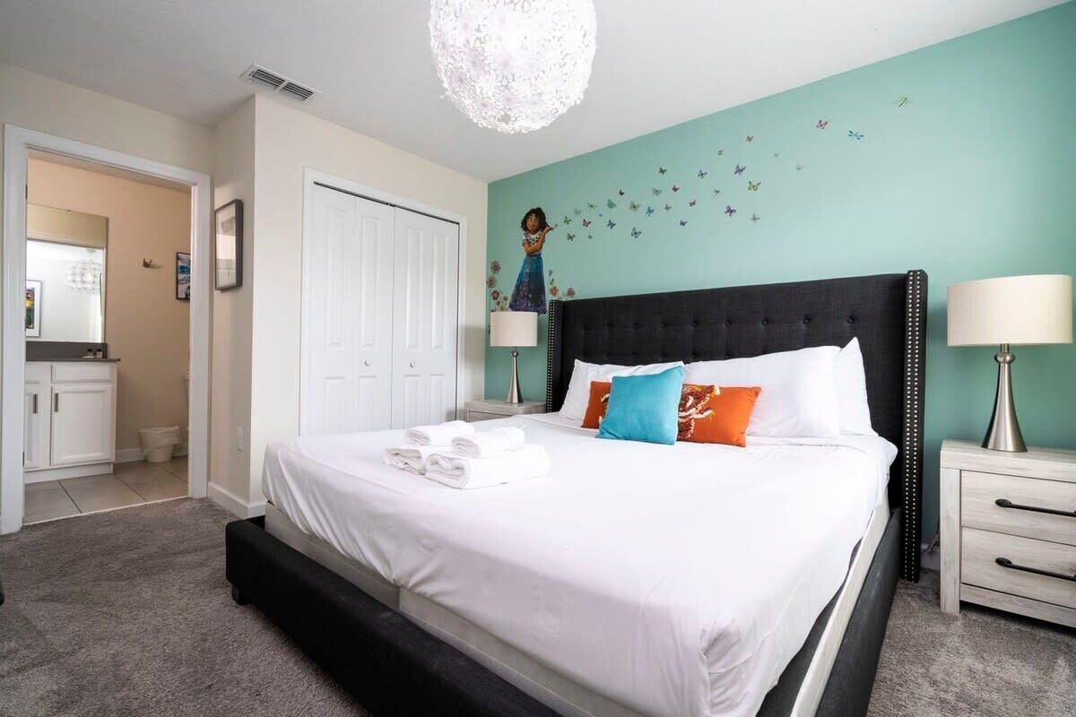 Une chambre à coucher comprenant un lit, une table de chevet, une lampe, un élément décoratif mural et une porte donnant sur une autre pièce.
