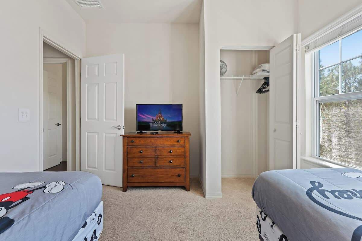 A bedroom with two beds, a dresser, a television, and a closet.