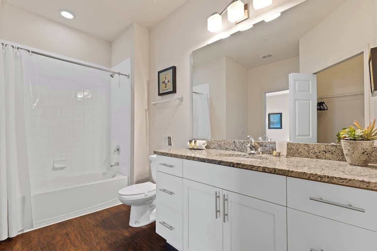 A modern bathroom with a walk-in shower, white toilet, and granite countertop.