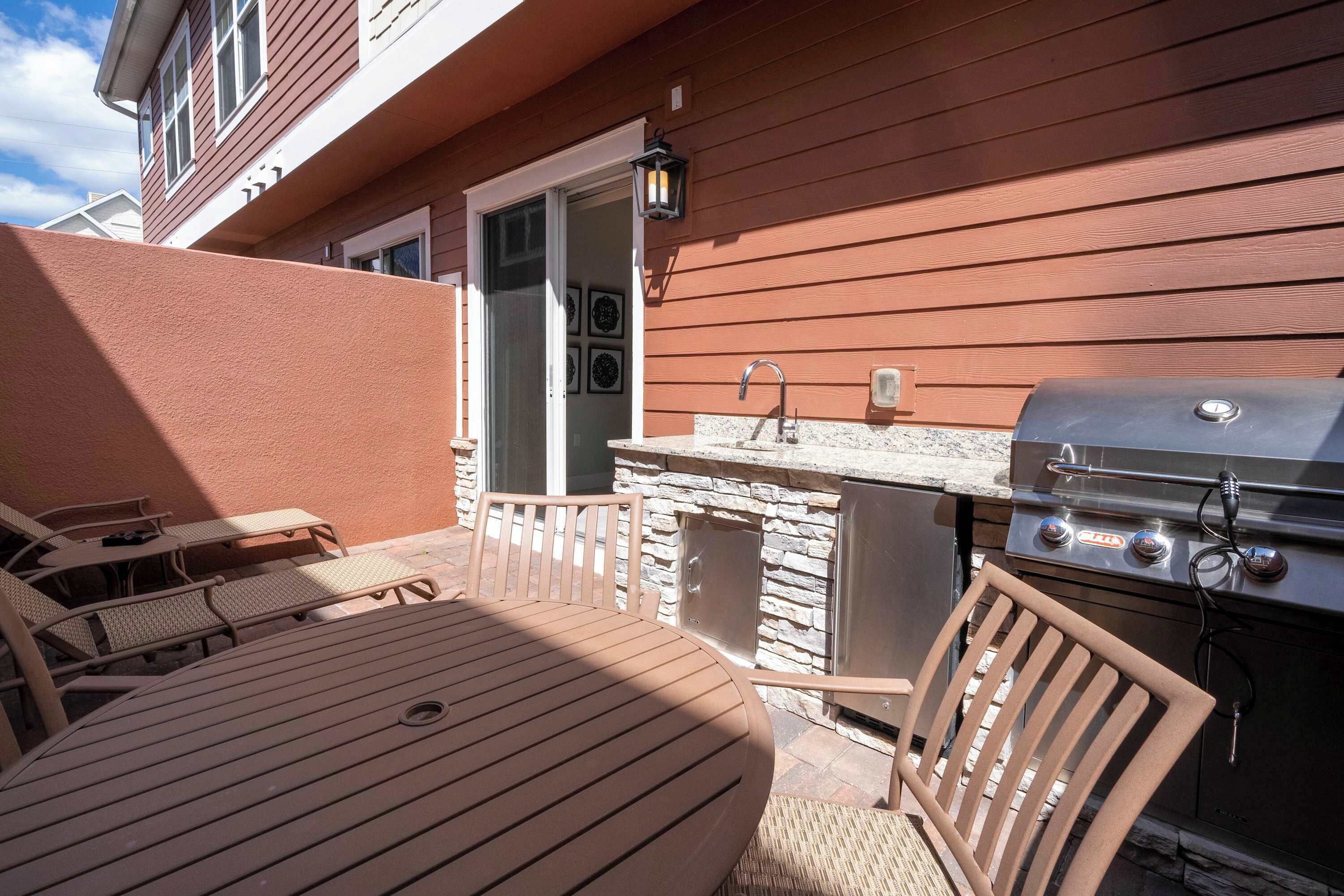 Eine Terrasse mit rundem Tisch und Stühlen, einem Grill und einer Steinmauer.