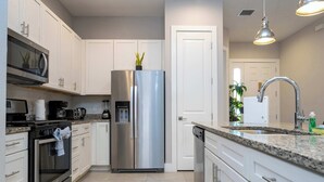 Une cuisine moderne dotée d’appareils électroménagers en acier inoxydable, de meubles blancs et de plans de travail en granit.