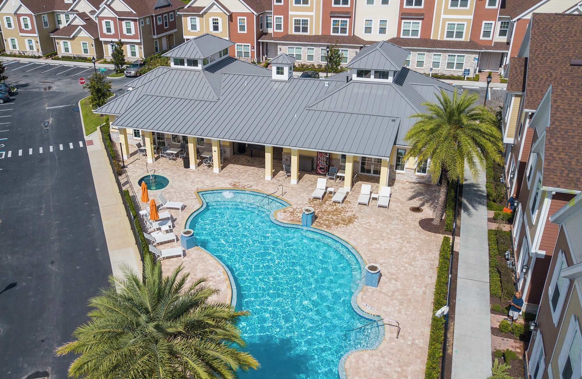 A residential building with a swimming pool, lounge chairs, and palm trees.