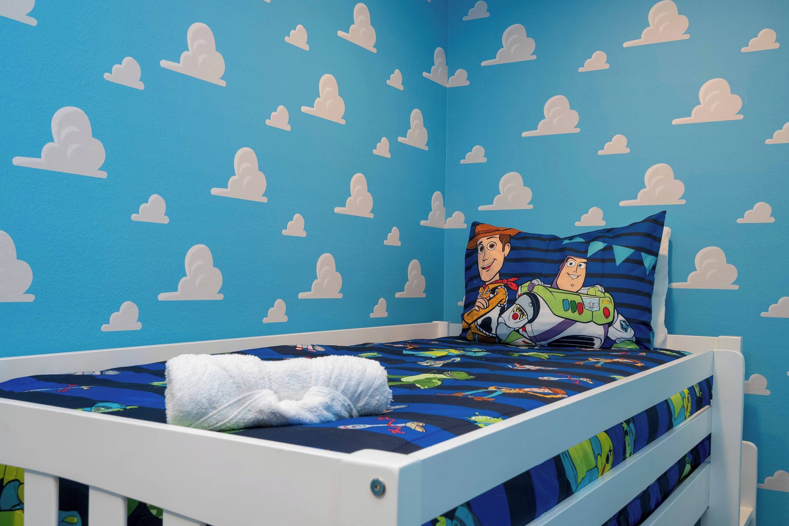 A child's bedroom with a blue wall, white cloud patterns, a bed with a Buzz Lightyear pillow, and a white blanket.