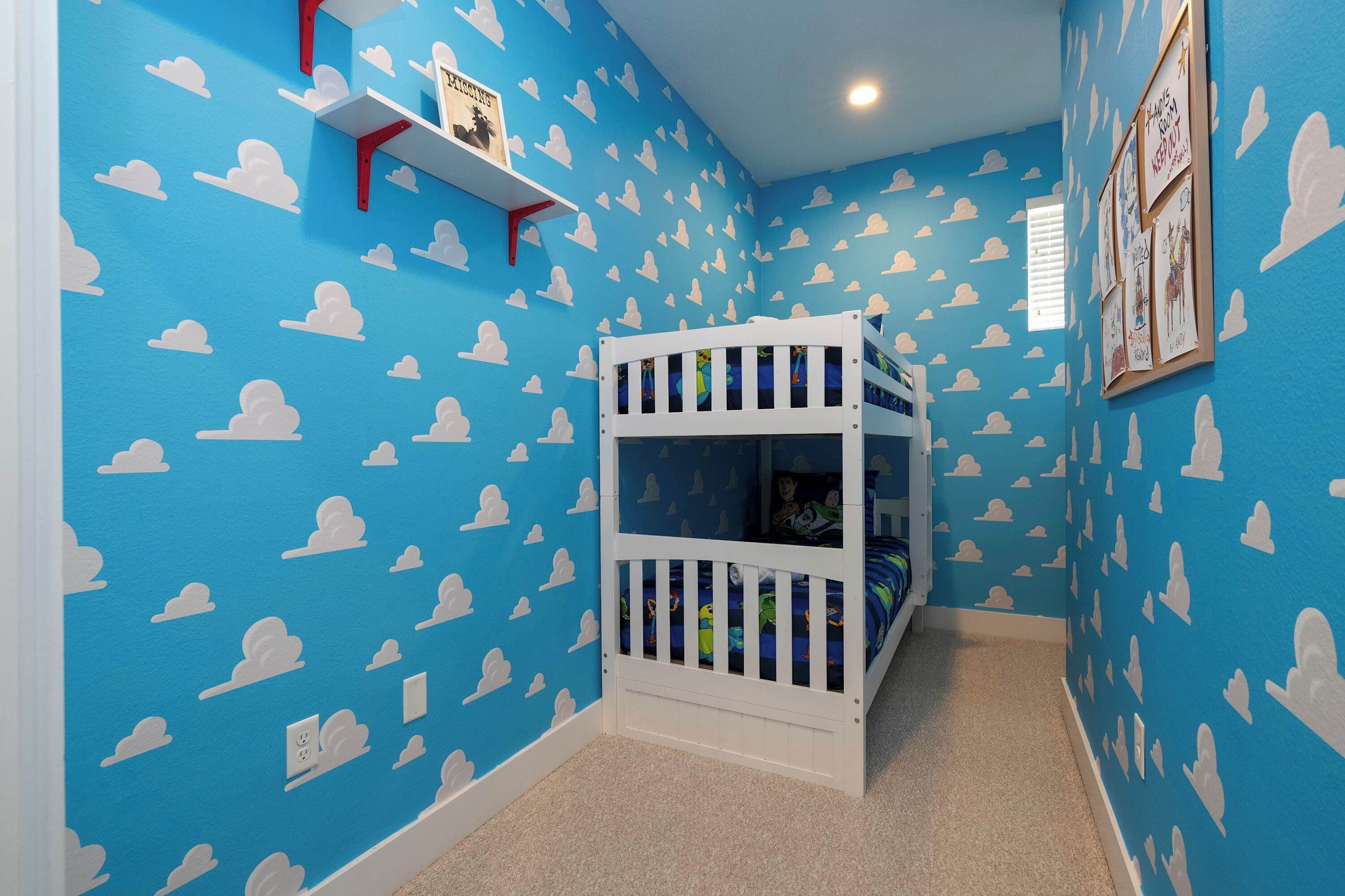 A room with a bunk bed, blue walls with cloud patterns, a white shelf, and a framed picture.