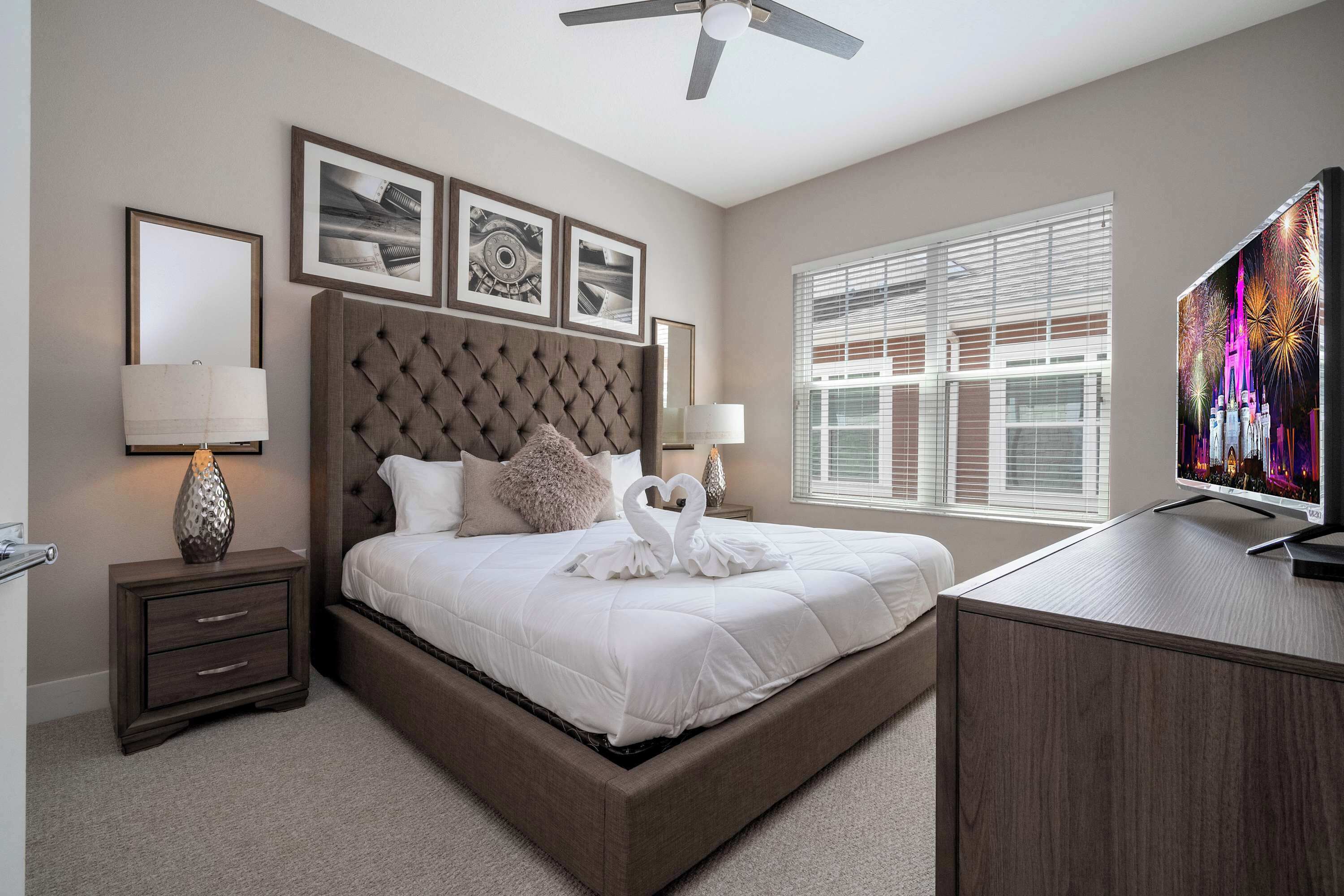 A bedroom with a large bed, a TV, a nightstand, and a window with blinds.