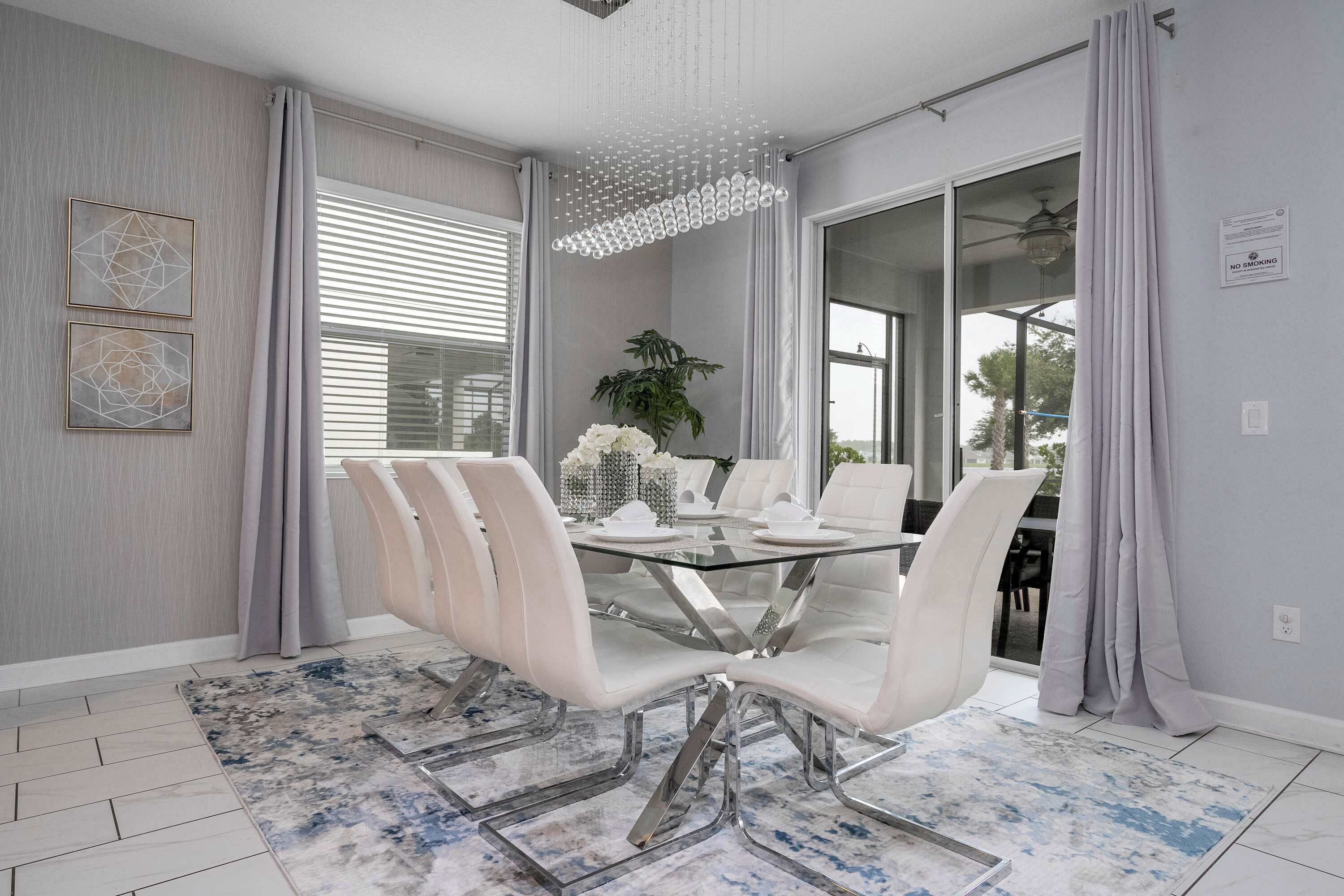 Un comedor moderno con una mesa de vidrio, sillas blancas y un tapete estampado.