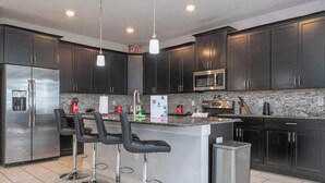 A modern kitchen with dark cabinets, stainless steel appliances, and a central island with bar stools. - Home 6bed , Themed Rooms, Game Room, Storey Lake (Kissimmee)