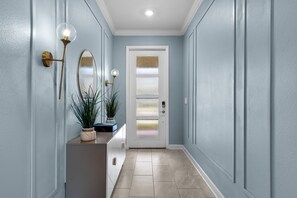 Un pasillo con paredes azul claro, una puerta blanca con paneles de vidrio esmerilado y una planta en una mesita consola.