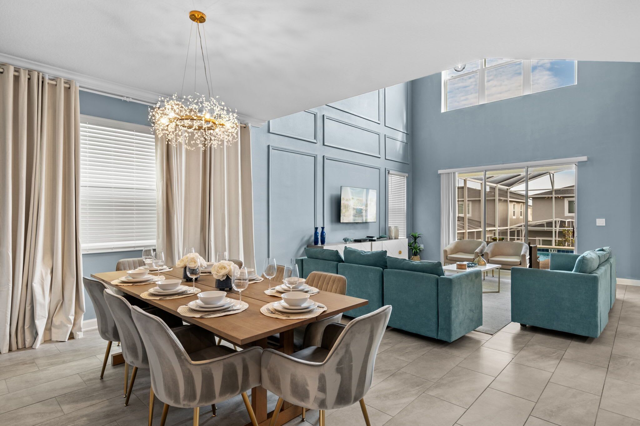 A modern living room with a dining area, teal sofas, and a chandelier.