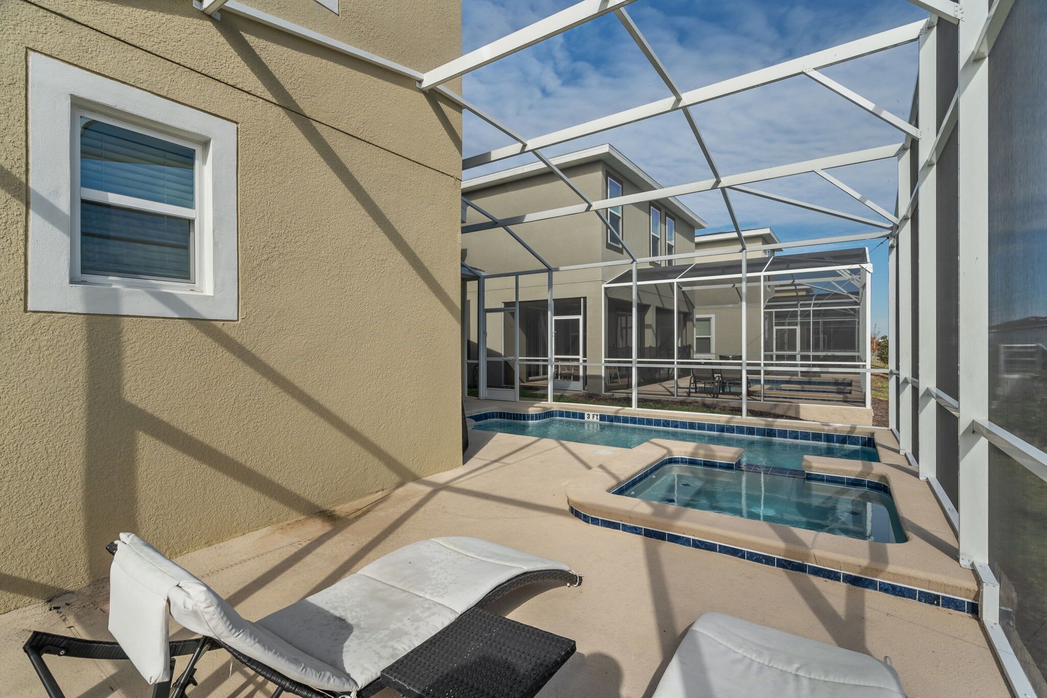 A pool area with lounge chairs, a hot tub, and a covered patio.