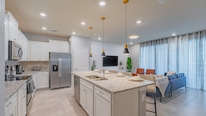 A modern kitchen with built-in appliances, a central island with a sink, and a dining area with a sofa and chairs. - Luxury Themed Bedrooms Haven (Davenport)