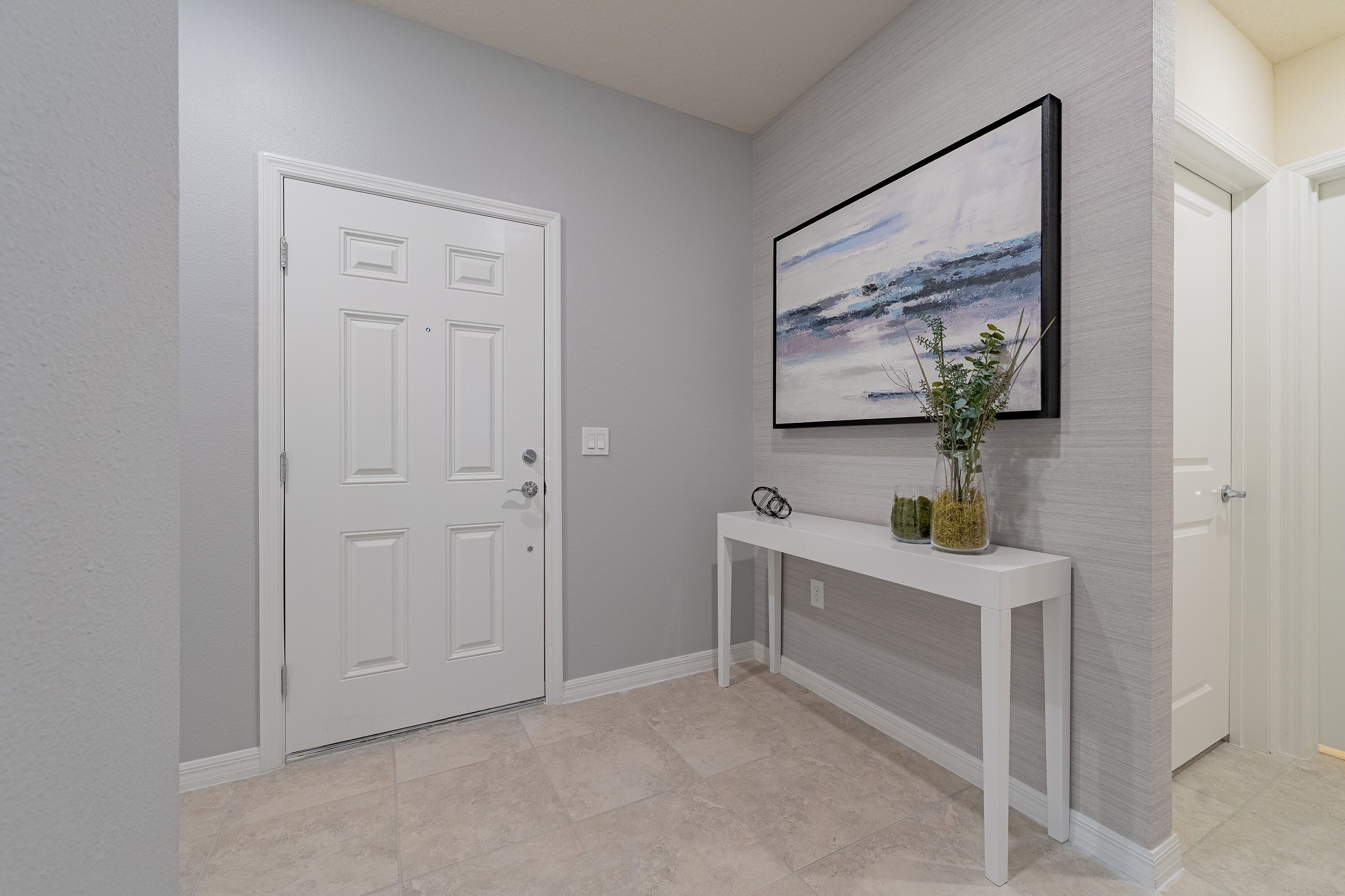 Un couloir avec une porte blanche, une console ornée d’objets décoratifs et un tableau encadré accroché au mur.