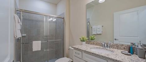 A modern bathroom with a glass-enclosed shower, a white toilet, a granite countertop, and a large mirror.