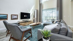 A modern living room with a flat-screen TV, grey sofas, a coffee table, and a staircase leading to a balcony. - Chic Home, Themed Bedrooms, Game Room, Best Spot (Kissimmee)